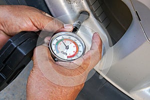 Hand holding pressure gauge for car tire pressure measurement.