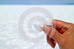 Hand holding pure white natural salt crystals with blurred Salar de Uyuni Salt Flats of Bolivia in background