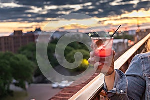 A hand holding a red alcoholic beverage at a Savannah, Georgia at sunset