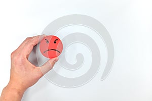 Hand holding a red angry face icon in white background with copy space. Anger management and bad customer service.