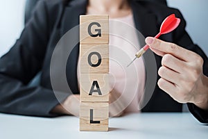 Hand holding red dart over Goal block. target, aim, objective, leadership, Business and marketing concept