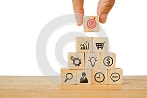 Hand holding red dartboard to place on top pyramid of business and finance icon on wooden cubes for target, goal, strategy