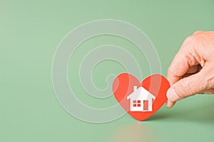 Hand holding red heart with home sign on green background for family home, homeless shelter and real estate, housing and mortgage