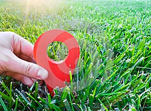 A hand is holding a red location marker in the green grass. The concept of tourism and travel. Navigation and exploration.