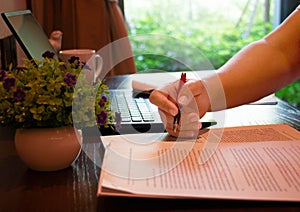 Hand holding red pen over blurred paperwork