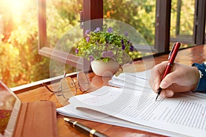 hand holding red pen over blurred paperwork for proofreading