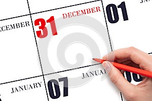 A hand holding a red pen and pointing on the calendar date December 31. Red calendar date, copy space, mockup.