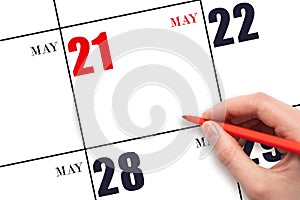 A hand holding a red pen and pointing on the calendar date May 21. Red calendar date, copy space, mockup.