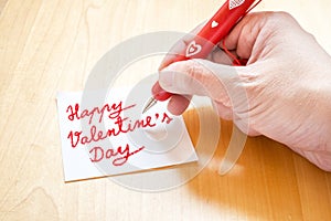 Hand holding red pen with white heart pattern, writing on blank