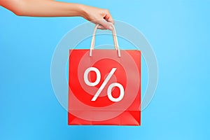 Hand holding red shopping bag with percentage sale sign on blue background