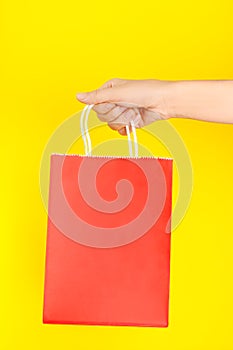 Hand holding red shopping or gift bag against yellow background