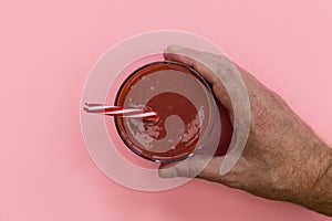 Hand holding red strawberry smoothie drink pink background