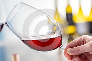 Hand holding red wine glass against light background.