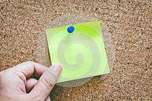 Hand holding reminder sticky note on cork board