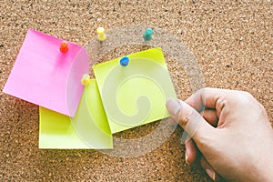 Hand holding reminder sticky note on cork board