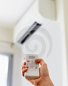 Hand holding remote control, adjusting temperature of air conditioner mounted on a white wall. Indooor comfort temperature.