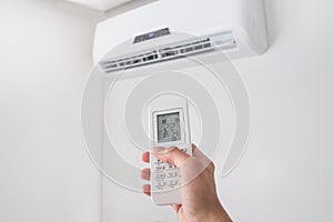 Hand holding remote control for air conditioner on white wall.