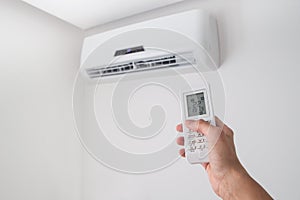 Hand holding remote control for air conditioner on white wall.