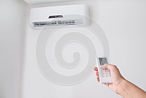 Hand holding remote control for air conditioner on white wall.