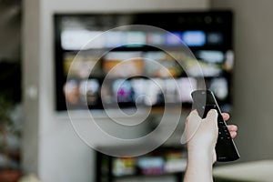 Hand holding remote control pointing to TV. Person watching smart television