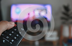 Hand holding remote control of a television. Hands pointing to tv screen set and turning it on or off select channel watching tv