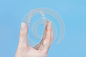 Hand holding removable invisible transparent aligner invisalign or plastic orthodontic braces retainer on blue