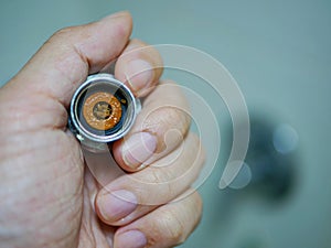 A hand holding a removed / disassembled part of a rain shower head getting clogged with mineral deposits