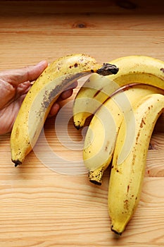 Hand holding ripe banana with brown spots on its peels