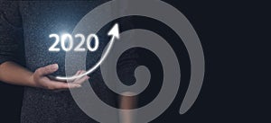 Hand holding a rising arrow with gologram 2020 year. Business people plan to increase business growth and add key growth in 2020