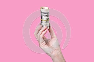 A hand holding a roll of money isolated on pink background