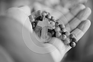 Hand holding Rosary in black and white background. Senior woman holding rosary with open hand with Jesus Christ Cross Crucifix.