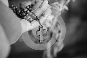 Hand holding Rosary in black and white background. Senior woman holding rosary with open hand with Jesus Christ Cross Crucifix.
