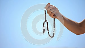 Hand holding rosary, praying to god on blue background, religious spirituality