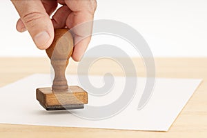 Hand holding a Rubber stamp and blank paper on wooden table