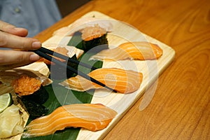 Hand holding salmon sushi using chopsticks - Steamed rice topped with fresh salmon sliced.