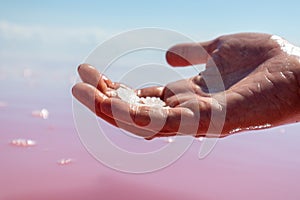 Hand holding salt crystals near pink water surface