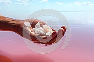 Hand holding salt crystals near pink water surface