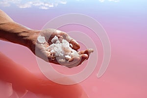 Hand holding salt crystals near pink water surface