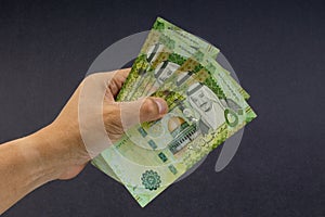 Hand holding saudi riyal bank notes on black background.