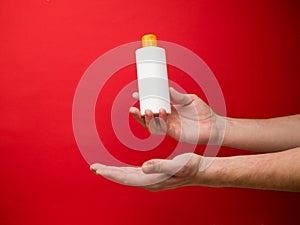 Hand holding shampoo bottle isolated on red background