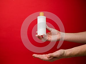 Hand holding shampoo bottle isolated on red background