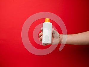 Hand holding shampoo bottle isolated on red background