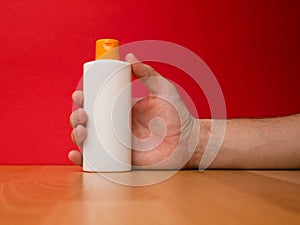 Hand holding shampoo bottle isolated on red background