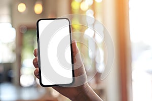 A hand holding and showing black mobile phone with blank white screen in modern cafe