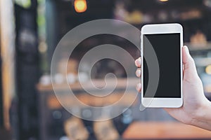 Hand holding and showing white mobile phone with blank black screen in modern loft cafe