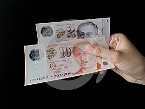 Hand holding a Singapore 10 and 2 dollars over black background