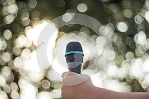 hand holding a single microphone against colourful background,singing contest.