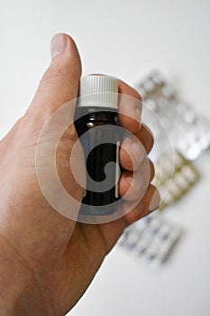Hand holding a small bottle with medicine with the background of different pills on a white table