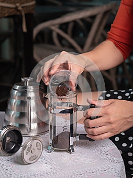 Hand holding small cup of ground coffee and pouring into a jar