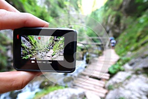 Hand holding small outdoor camera, filming photographing or taking pictures of tourists on wooden walk path in Prosiecka Valley